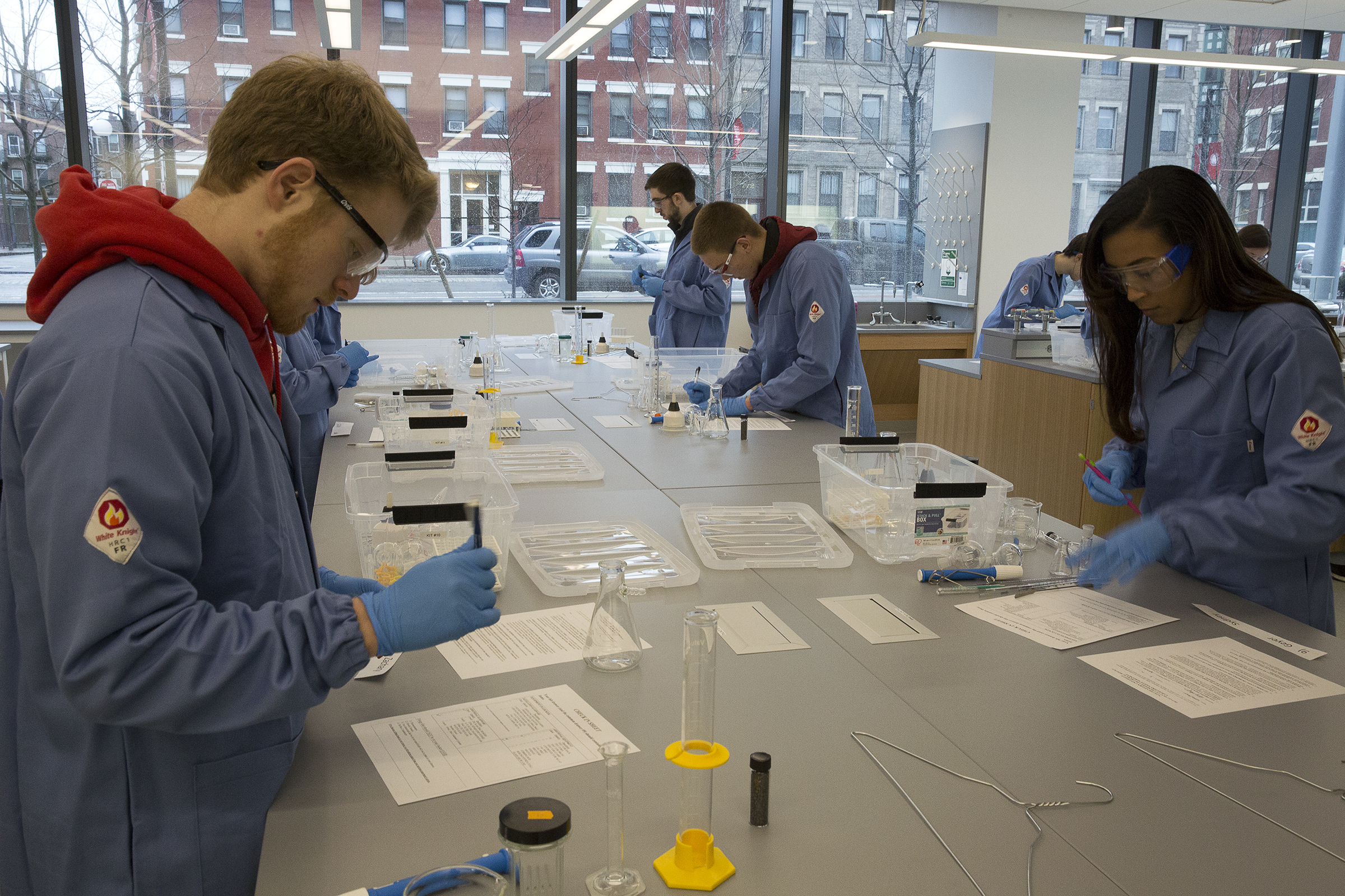Several students work at a lab bench with large windows behind them.