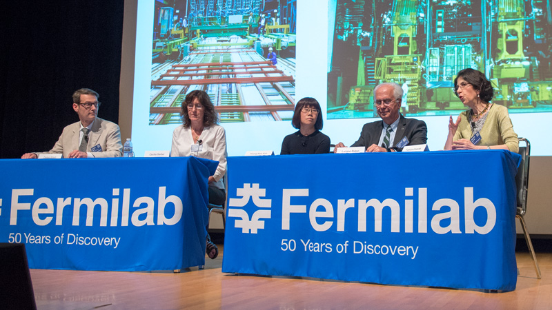 Four people sitting on a panel on a stage with a Fermilab tablecloth draped over the table.