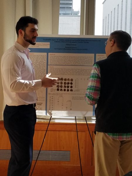 Michael Mallouh talks with another person while standing in front of a scientific poster.