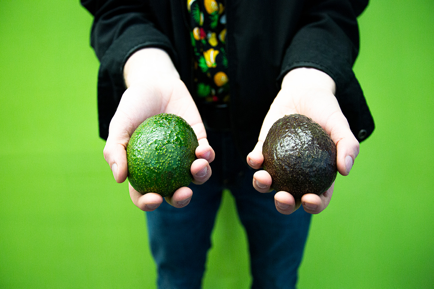 Person holds two avocado in a green room