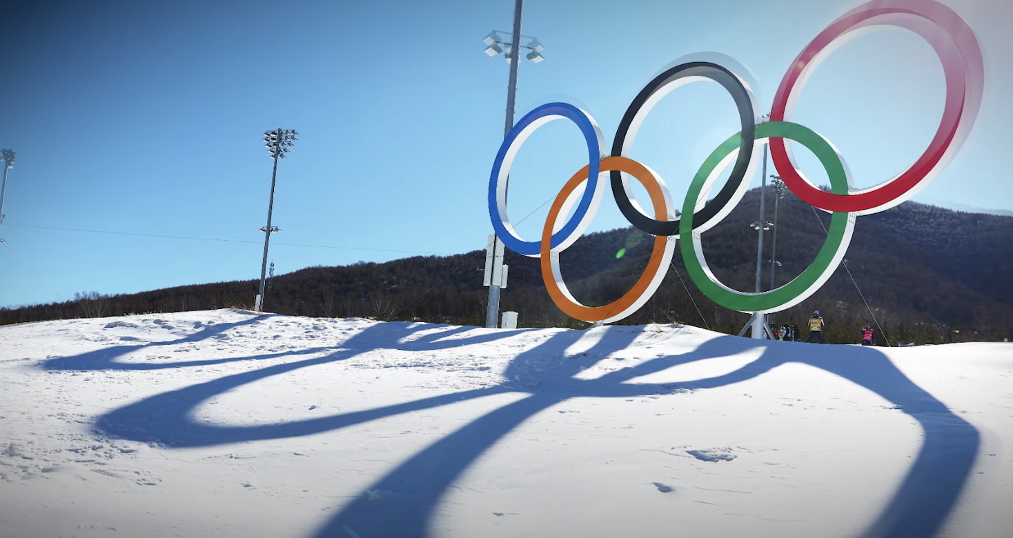 the olympics rings outside on a snowy hill, casting big shadows