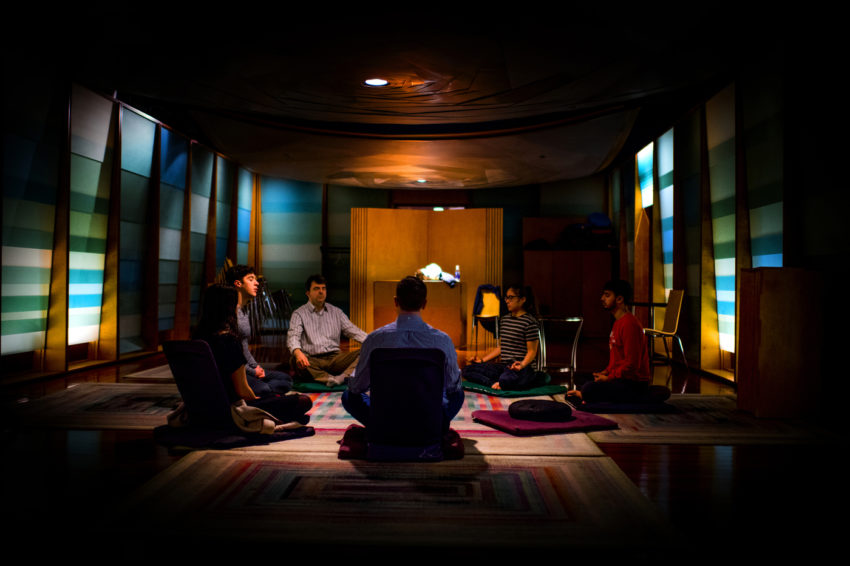 a group of people in dim lighting, sitting criss-cross and meditating in the Center for Spirituality Dialogue and Service, Sacred Space