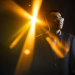 dacheng lin poses for a headshot with a glare of light behind him