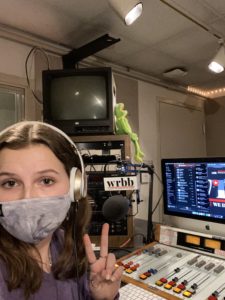 katherine wears a mask and headphones sitting in front of a computer and radio equipment