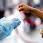 hands reach out to put a covid swab into a tube in the gloved hands of another at cabot testing center