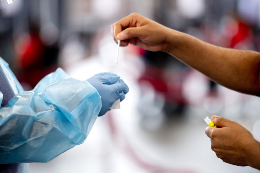 hands reach out to put a covid swab into a tube in the gloved hands of another at cabot testing center