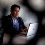 Mauricio Santillana sits at a desk typing on his macbook