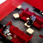 two people sit among empty red chairs and couches