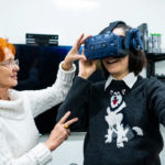Dagmar Sternad, a women, is seen holding up another person who has a pair of VR headsets on.