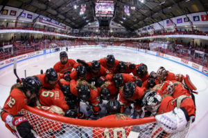 Women's ice hockey team huddled up by the goalie.