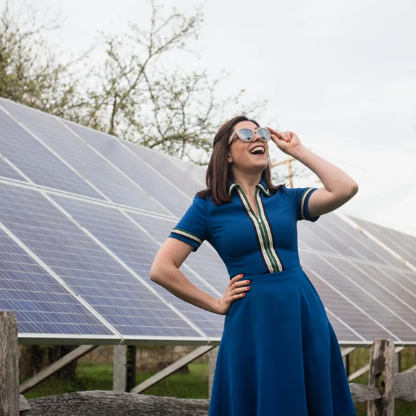 Sophie Shrand stands in front of solar panels and looks towards the sun while wearing sunglasses.