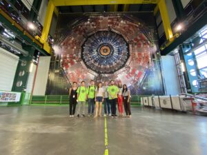 A group of people pose in front of a huge particle accelerator. 