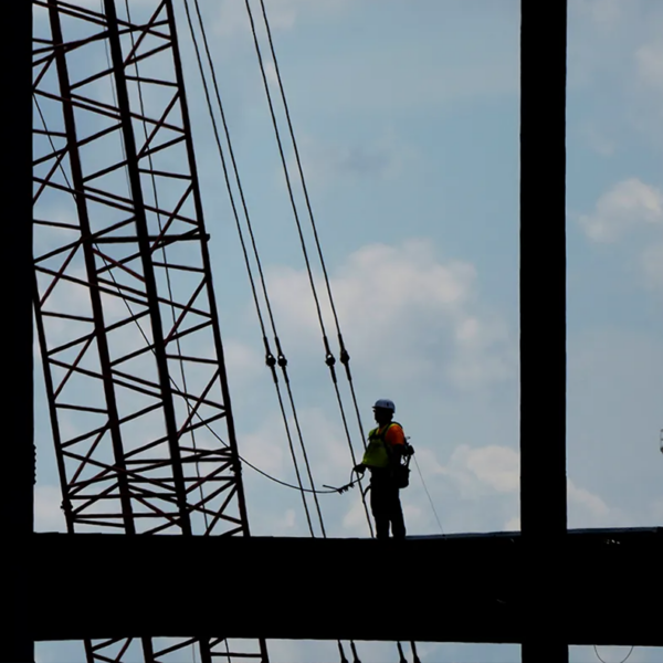 A construction worker stands on a beam in the air.