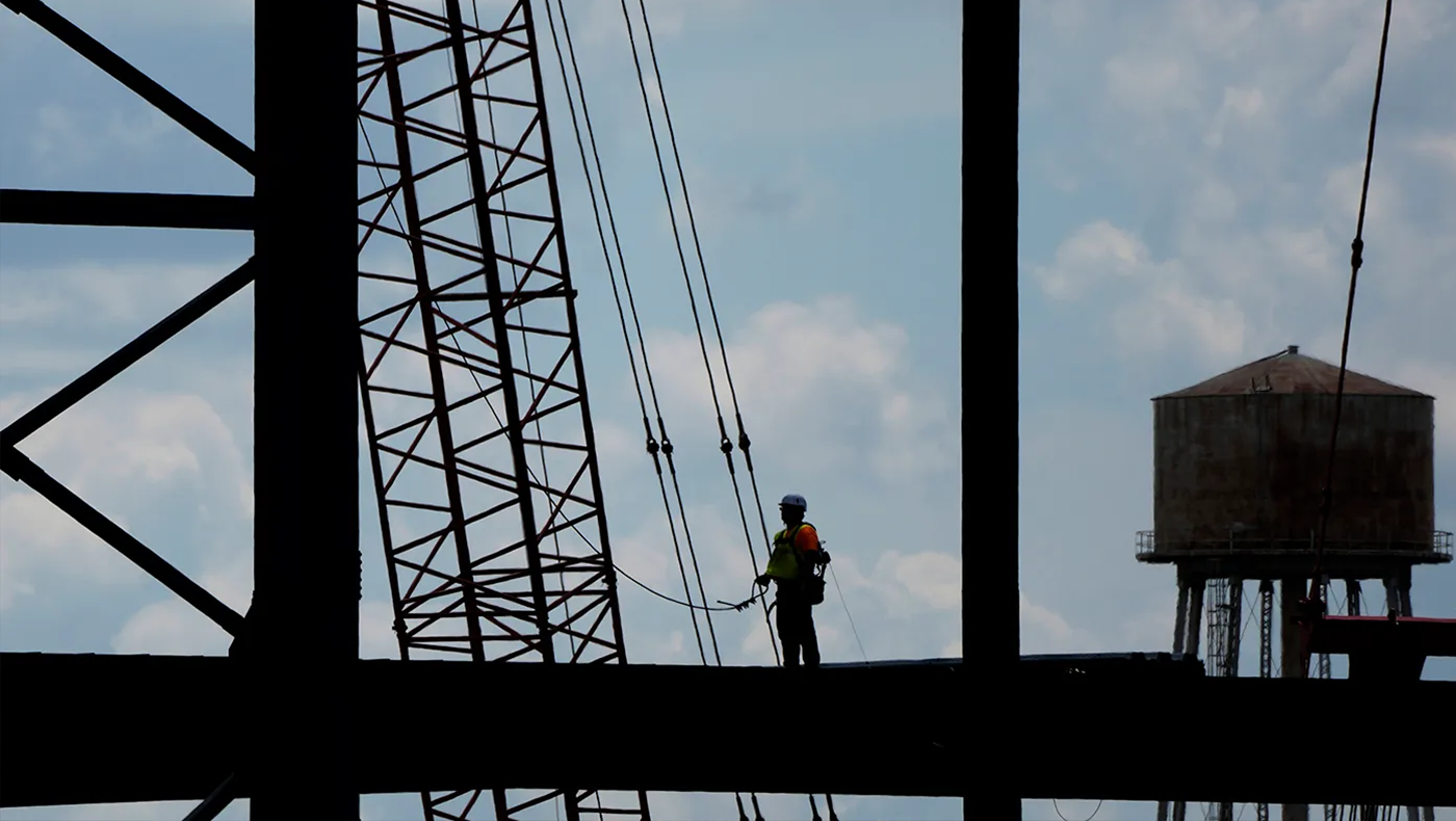 A construction worker stands on a beam in the air.