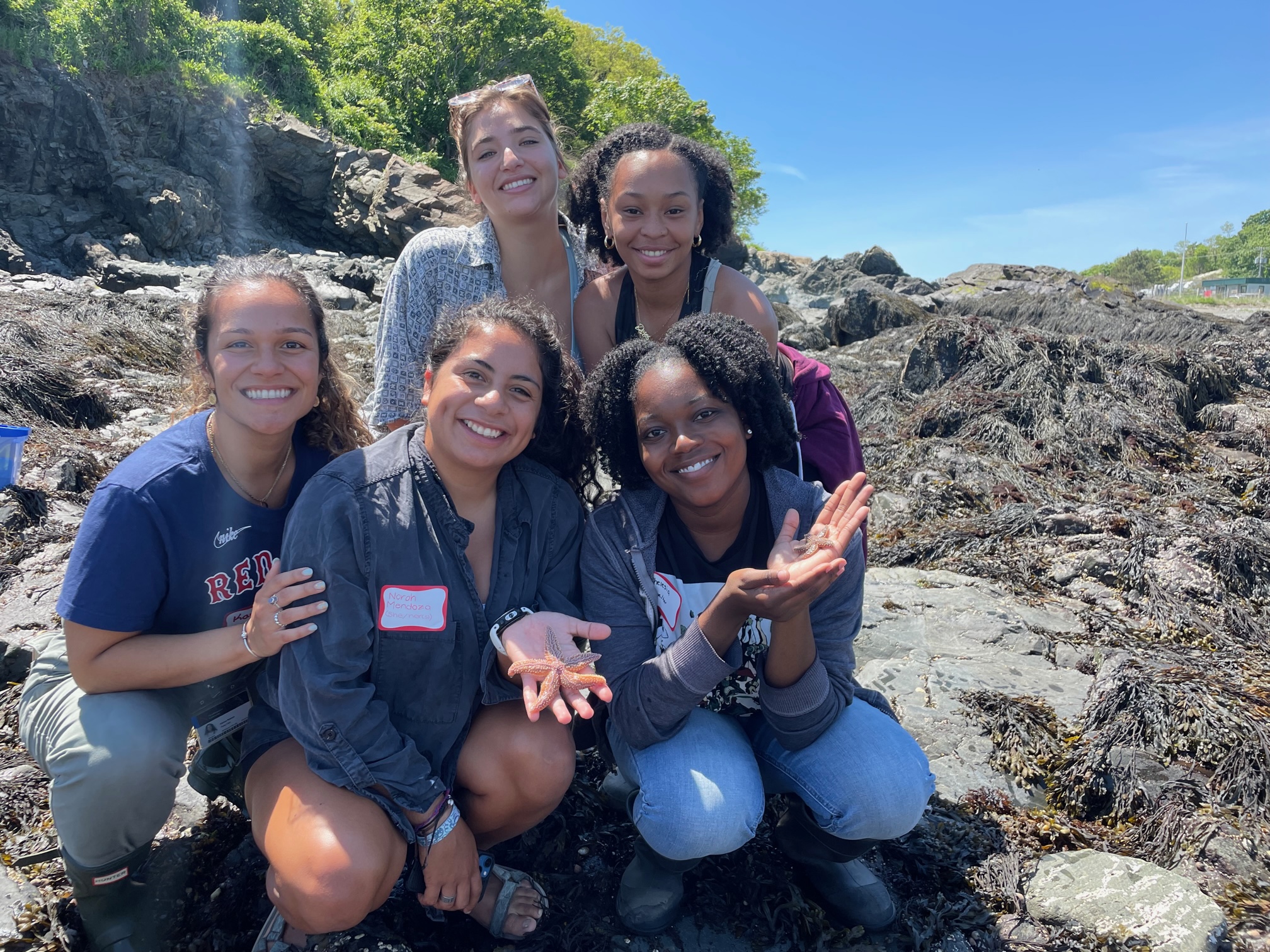 A group of students gathered on a rocky beach. Two are displaying starfish in the palms of their hands.