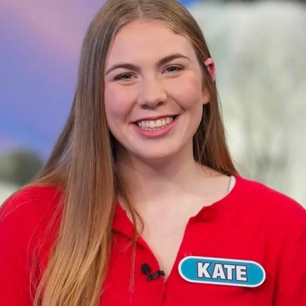 Portrait of a young women wearing a red sweater with a name tag that says Kate. Background is blurred but is for of purple and gray.