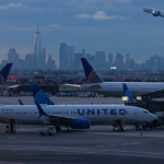 United plane in the forefront of a city scape with other planes in the background. Everything is very blue and gray.