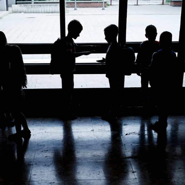 Backlit photo of a group of children in backpacks in front of a window.