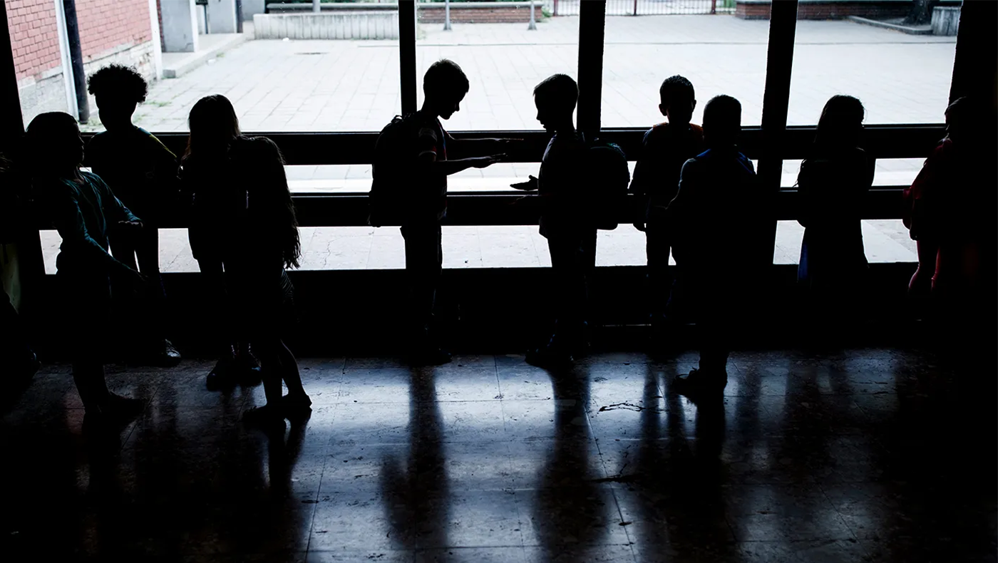 Backlit photo of a group of children in backpacks in front of a window.