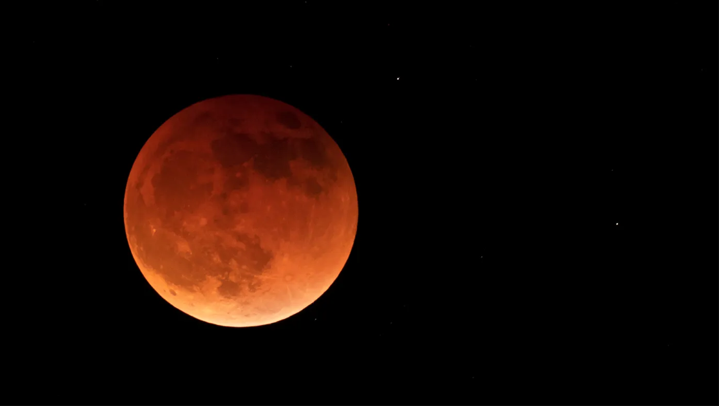 Redish orange shot of the moon on a black background. The details of the moons surface are fairly clear.