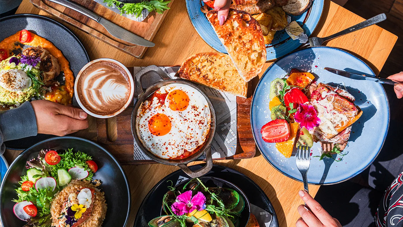 Overhead picture of for on a table. Food is very colorful and there are hands with utensils in them.